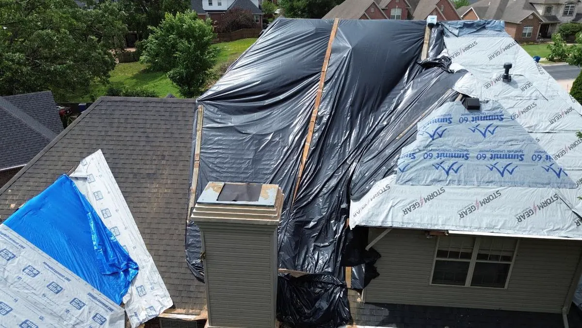 House roof covered with a black emergency tarp after storm damage
