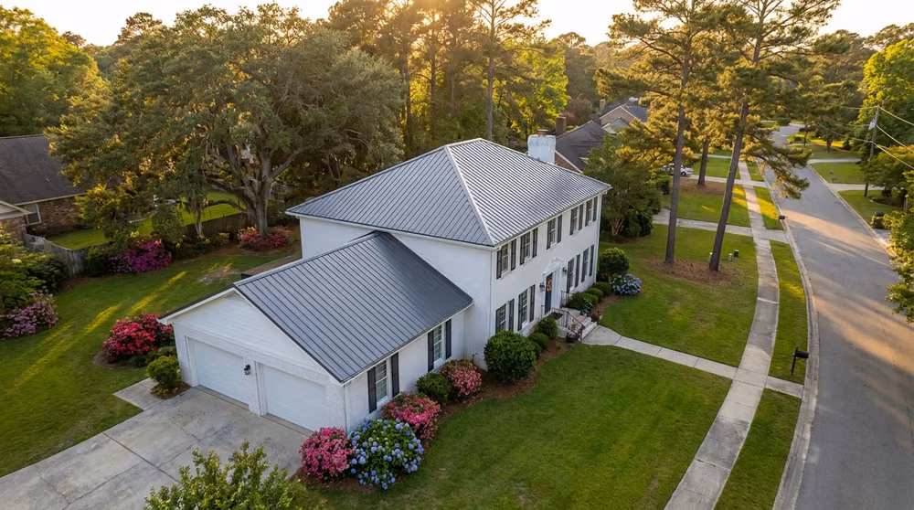 Drone view of a white brick two-story house and garage with a dark standing-seam metal roof
