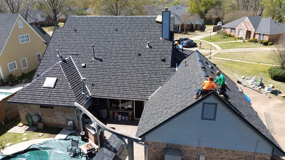 Drone view of two roofers working on a new dark roof over a brick house