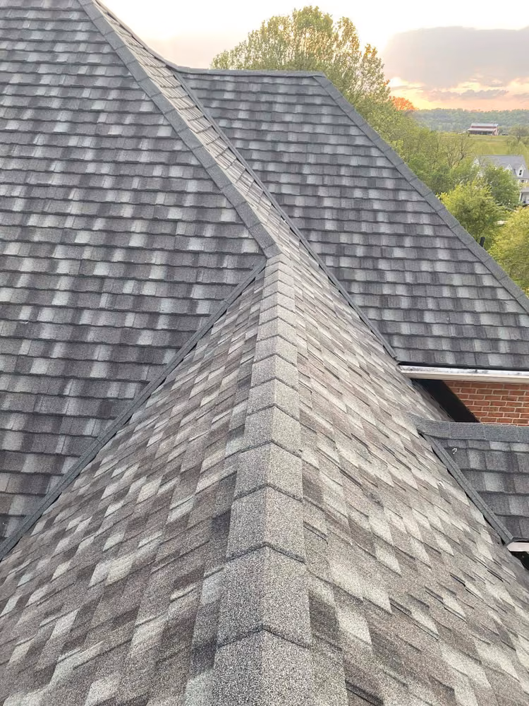 Gray architectural shingles covering the hips and a valley of a brick house at sunset