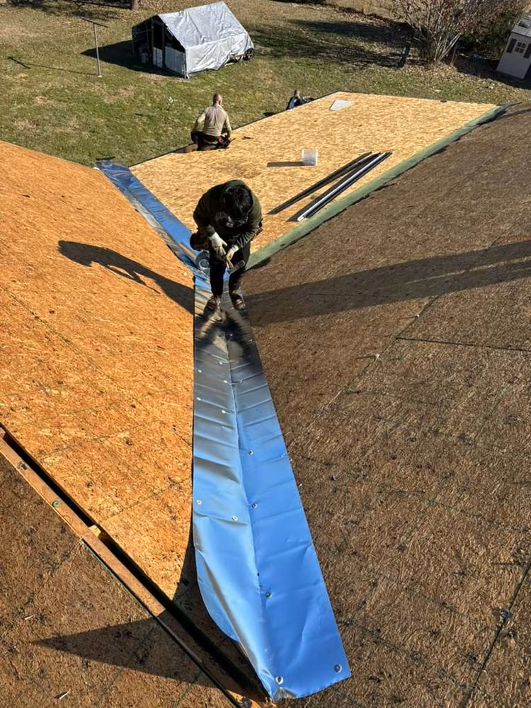 Roofer laying metal valley flashing over new roof decking