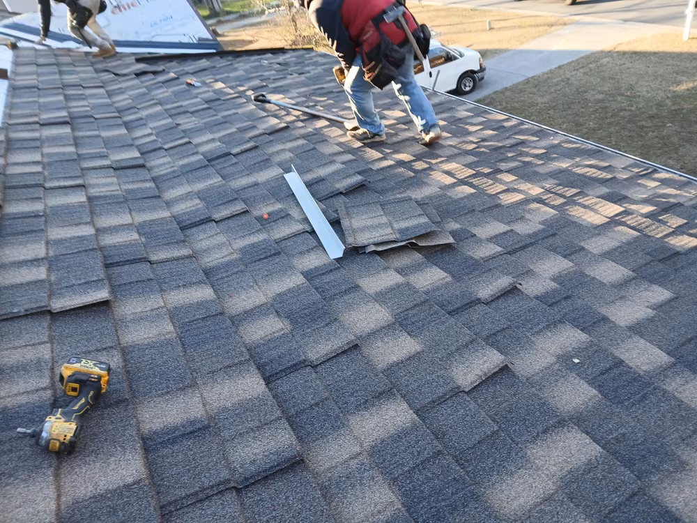 Roofer working his way across a new roof with a length of metal trim beside him