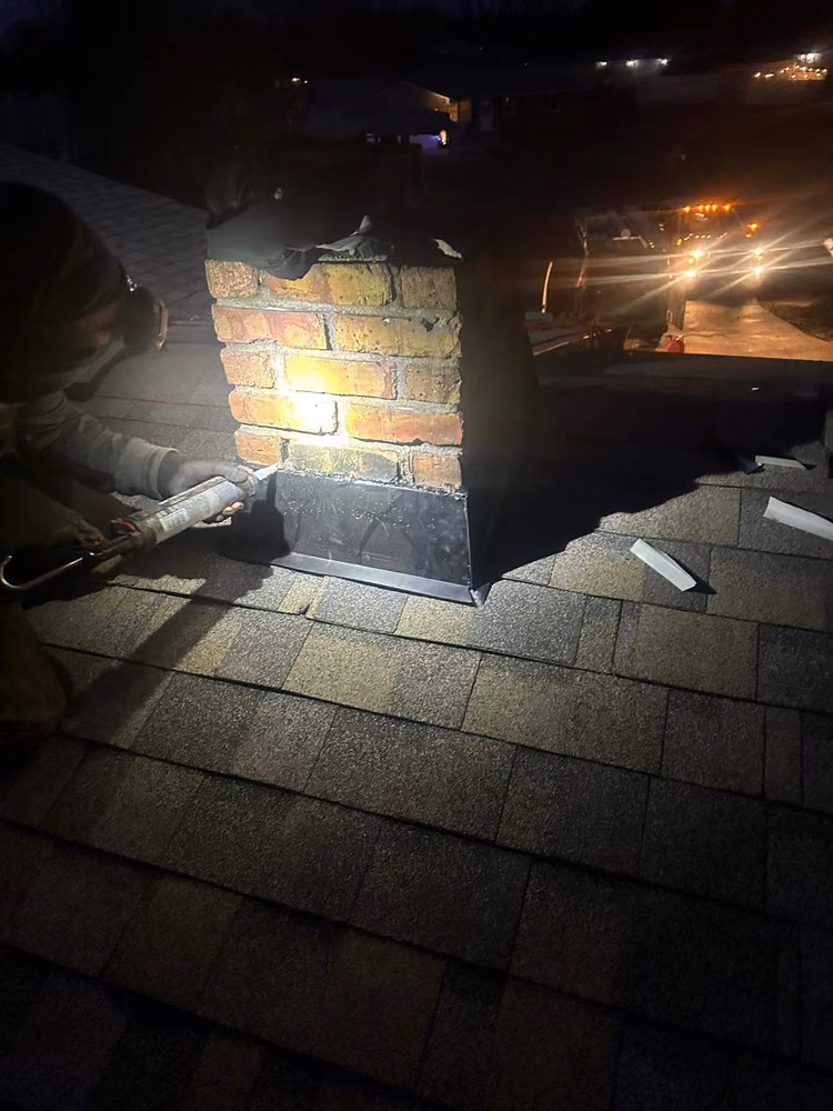 Roofer sealing new chimney flashing at night by the light of a headlamp