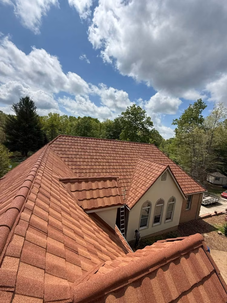 Terracotta stone-coated steel tile roof on a cream stucco house with arched windows, a ladder at the eave