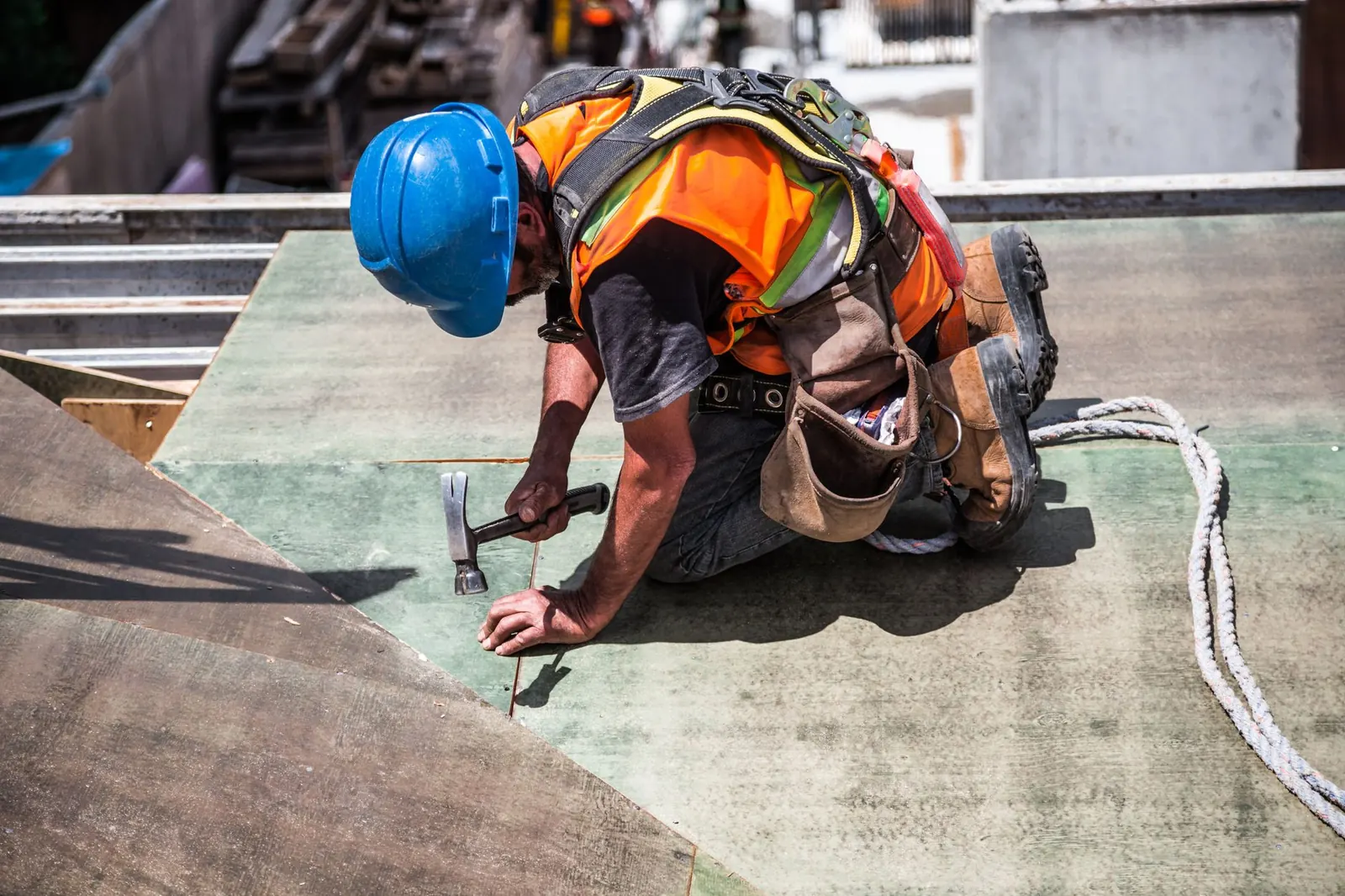 Roofer in a hard hat and safety harness nailing down roof decking