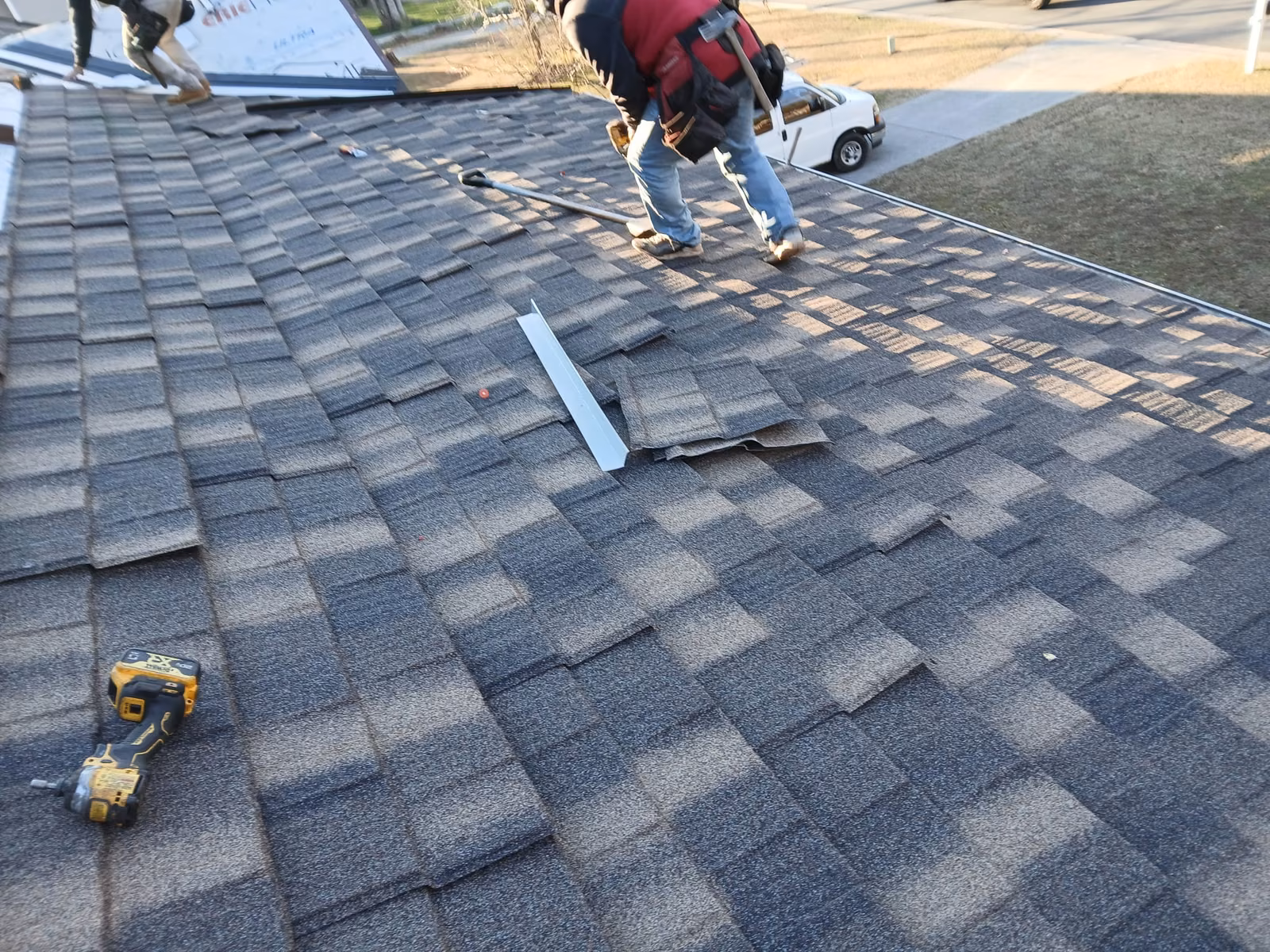 Roofers on a shingle roof with a nail gun, loose shingles, and a strip of flashing laid out