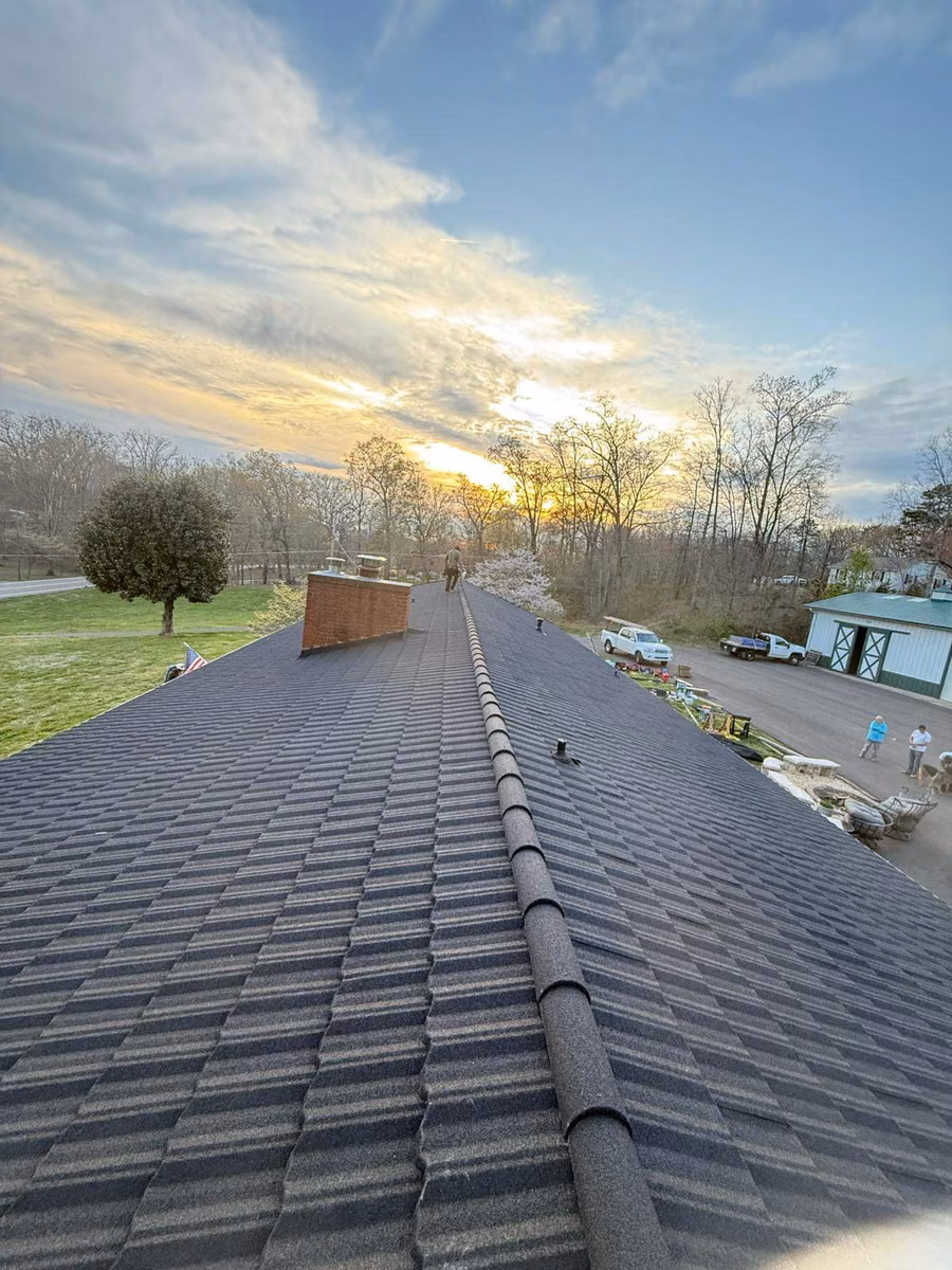 Stone-coated steel shake roof with a rounded ridge cap at sunset