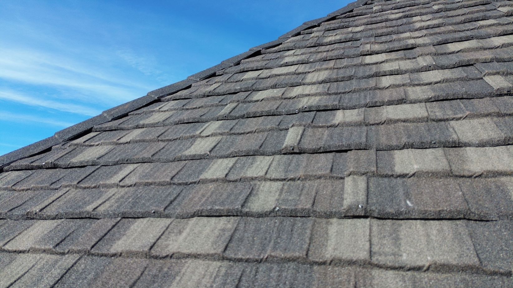Close view of gray stone coated steel roof panels in a shake style against a blue sky