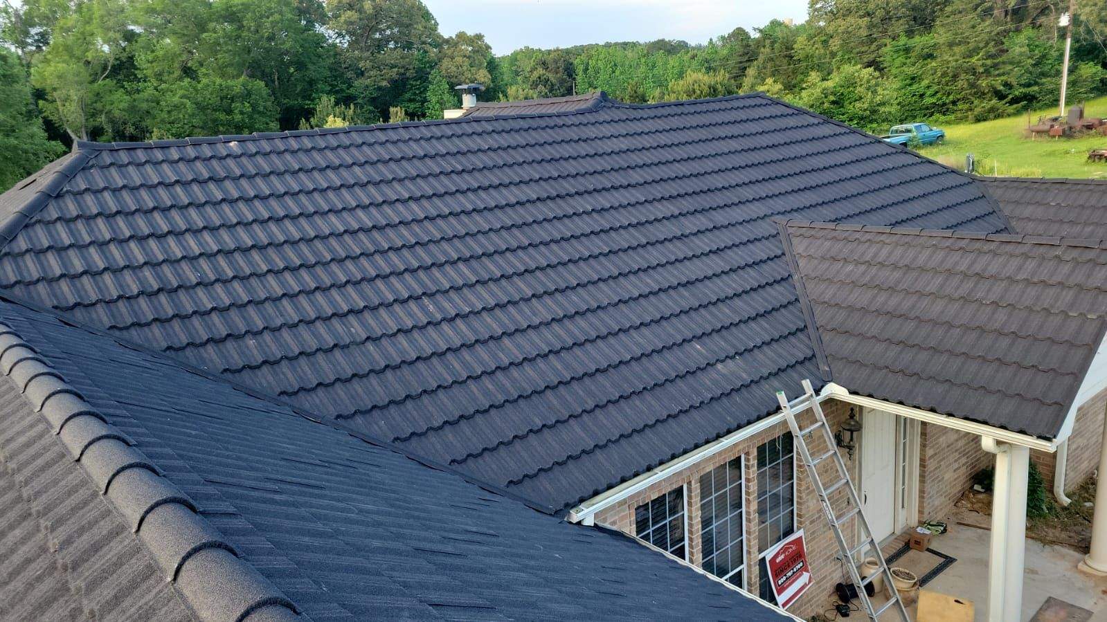 Black stone coated steel tile roof on a brick house, seen from above, with a ladder at the front porch
