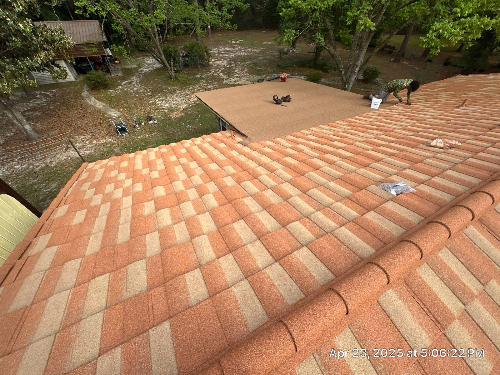 Terracotta stone coated steel tile with a barrel ridge cap, and a roofer working on a lower roof section covered in underlayment