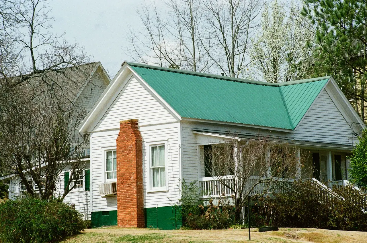 Green standing seam metal roof on a white clapboard house with a brick chimney